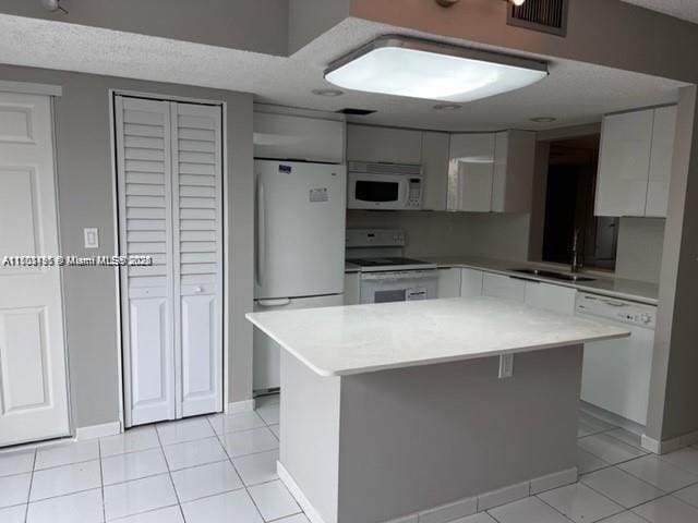 kitchen with light tile patterned floors, white appliances, a kitchen island, and sink