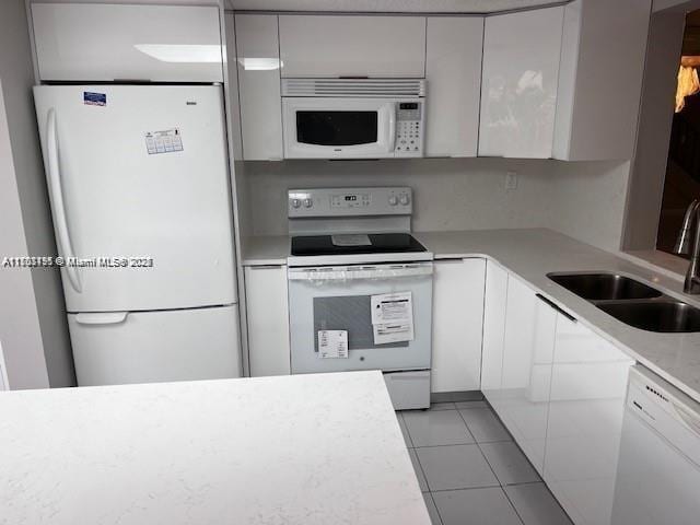 kitchen featuring white cabinets, sink, light tile patterned floors, and white appliances