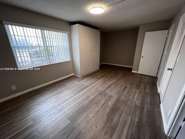 unfurnished bedroom featuring a textured ceiling, dark wood-type flooring, and a closet