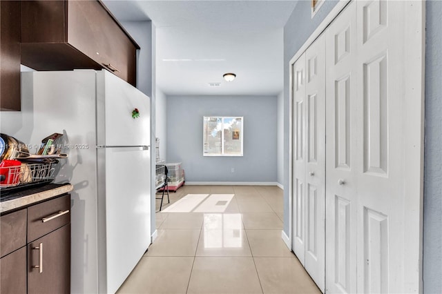 kitchen featuring dark brown cabinetry, light tile patterned floors, and white refrigerator