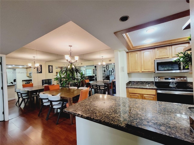 kitchen with light brown cabinets, dark wood-type flooring, decorative light fixtures, a notable chandelier, and stainless steel appliances