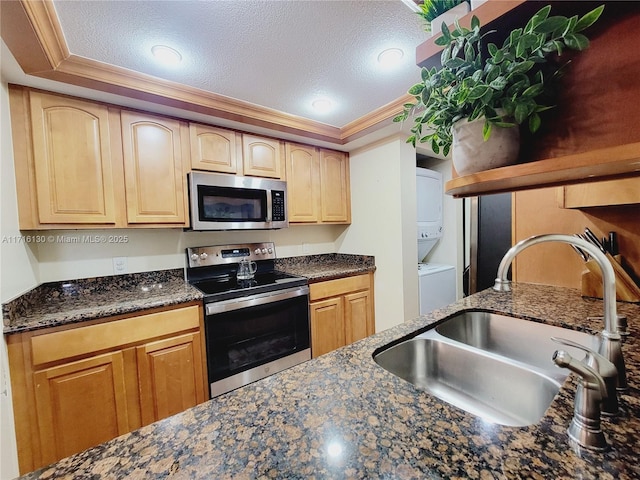 kitchen with sink, stacked washer and dryer, ornamental molding, a textured ceiling, and stainless steel appliances