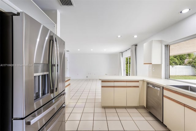 kitchen featuring sink, light tile patterned floors, kitchen peninsula, stainless steel appliances, and cream cabinetry