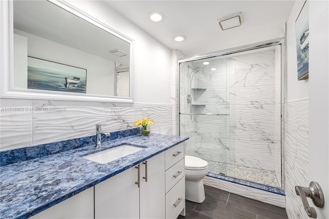 bathroom with vanity, toilet, an enclosed shower, and tile walls