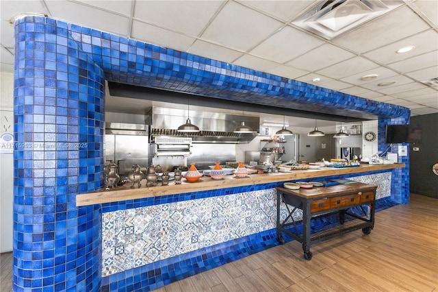 bar featuring a drop ceiling, wood counters, built in fridge, hardwood / wood-style floors, and pendant lighting