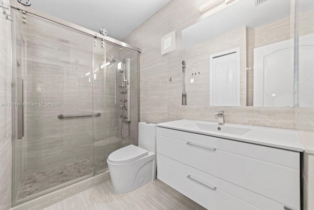 bathroom featuring vanity, toilet, a shower with shower door, and tile walls