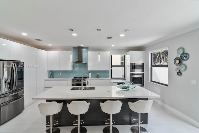 kitchen featuring stainless steel appliances, sink, wall chimney range hood, decorative light fixtures, and white cabinetry