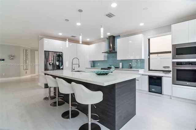 kitchen with white cabinets, wall chimney exhaust hood, appliances with stainless steel finishes, decorative light fixtures, and beverage cooler