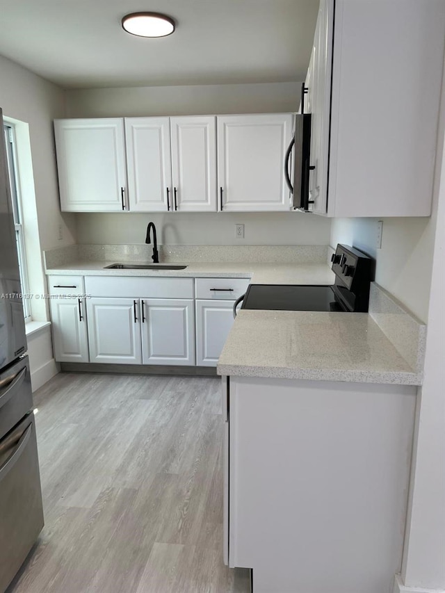 kitchen with light stone countertops, white cabinetry, sink, range with electric cooktop, and light hardwood / wood-style floors