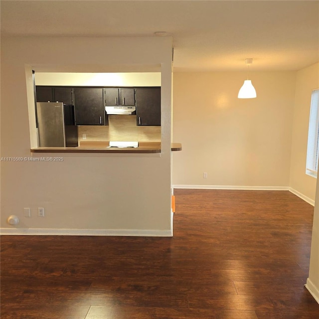 interior space with pendant lighting, stainless steel fridge, dark hardwood / wood-style flooring, decorative backsplash, and kitchen peninsula