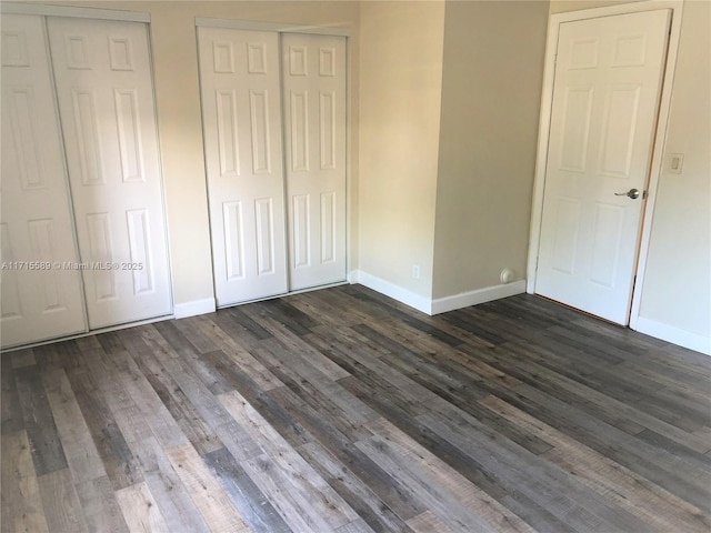 unfurnished bedroom with two closets and dark wood-type flooring