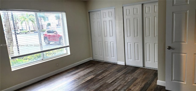 unfurnished bedroom featuring multiple windows, dark wood-type flooring, and two closets