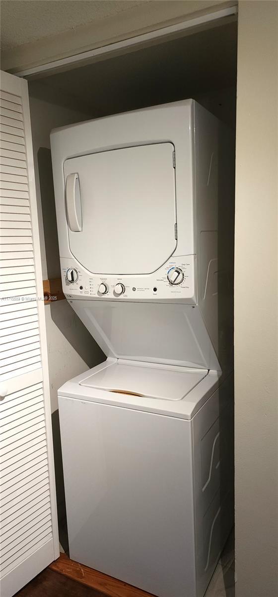 laundry area featuring stacked washer and clothes dryer and dark hardwood / wood-style floors