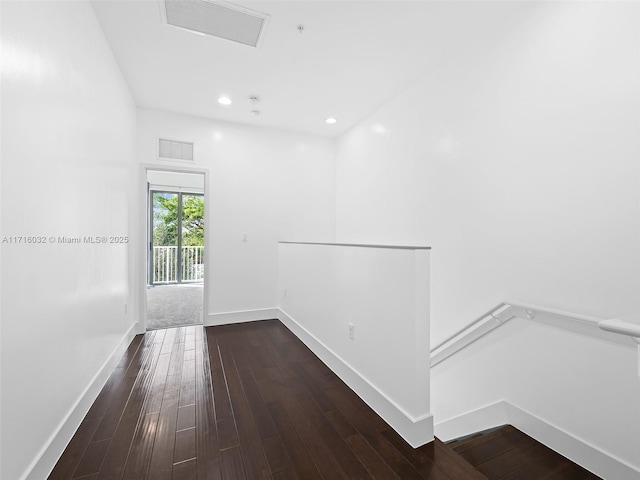 hallway featuring baseboards, visible vents, wood finished floors, and an upstairs landing