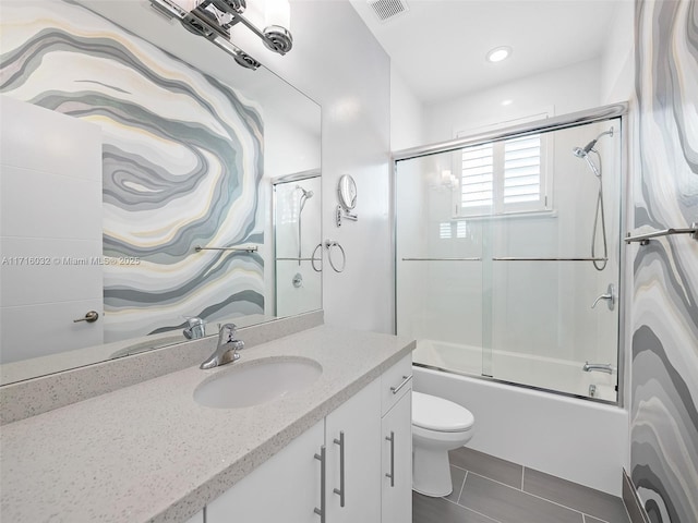 bathroom featuring toilet, vanity, visible vents, combined bath / shower with glass door, and tile patterned floors