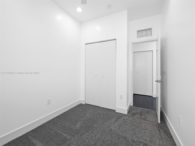 unfurnished bedroom featuring a closet, dark carpet, visible vents, and baseboards