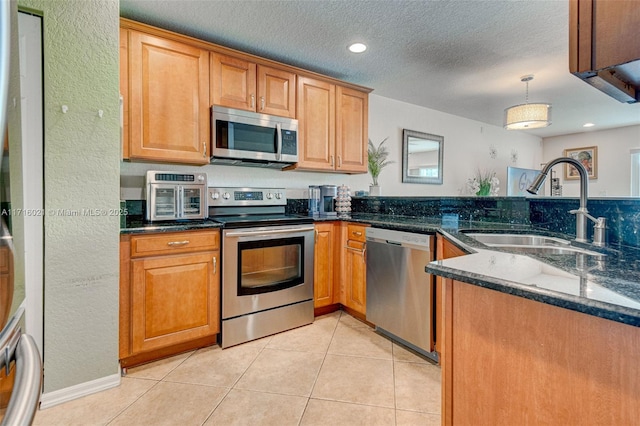 kitchen featuring appliances with stainless steel finishes, dark stone counters, sink, hanging light fixtures, and light tile patterned flooring