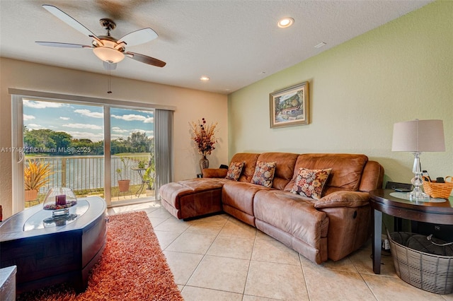 tiled living room featuring a textured ceiling, a water view, and ceiling fan