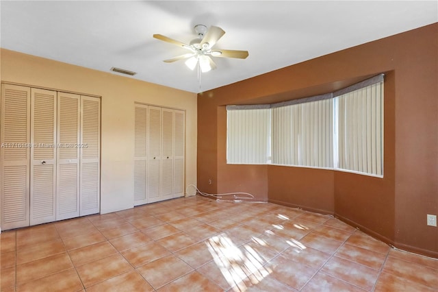 unfurnished bedroom featuring ceiling fan, light tile patterned floors, and two closets