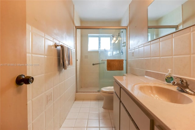 bathroom with vanity, a shower with door, tile patterned floors, toilet, and tile walls