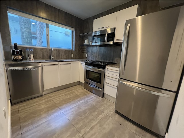 kitchen featuring light tile patterned floors, appliances with stainless steel finishes, white cabinets, and a sink