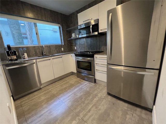 kitchen with stainless steel appliances, dark countertops, white cabinets, and a sink