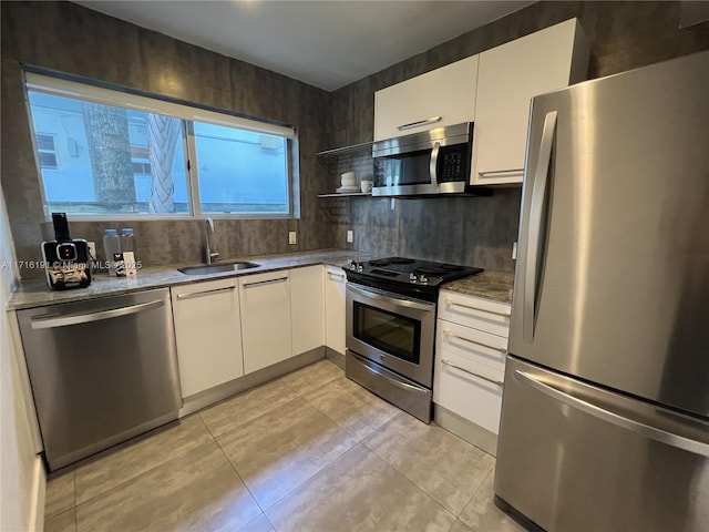 kitchen with light tile patterned floors, appliances with stainless steel finishes, white cabinets, and a sink