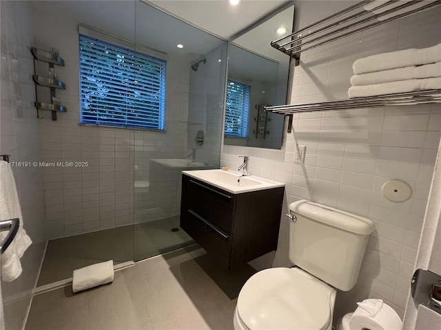 bathroom featuring tile patterned flooring, toilet, tiled shower, vanity, and tile walls