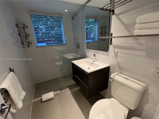 bathroom with toilet, tiled shower, vanity, and tile walls