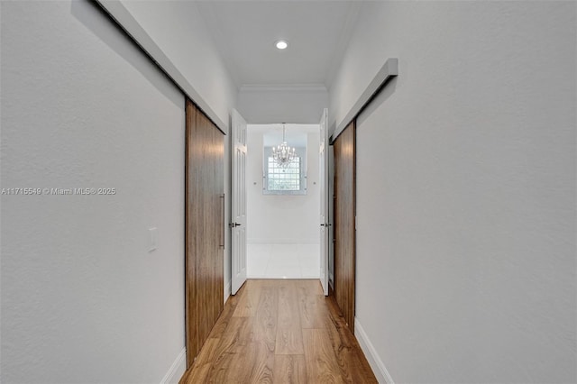 corridor featuring crown molding, light hardwood / wood-style flooring, and a chandelier