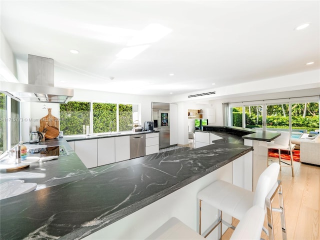 kitchen featuring white cabinetry, dishwasher, a kitchen bar, island exhaust hood, and kitchen peninsula