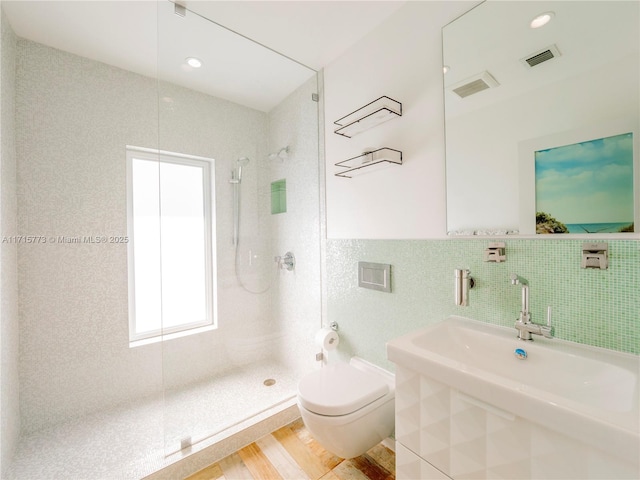 bathroom featuring hardwood / wood-style floors, toilet, tiled shower, tile walls, and sink