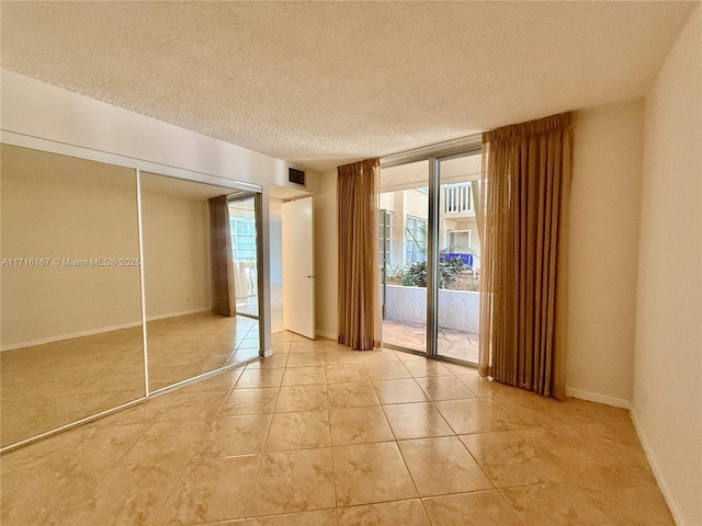 unfurnished bedroom featuring access to exterior, light tile patterned floors, a textured ceiling, and a closet