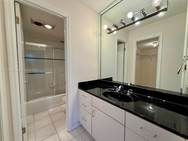 full bathroom featuring a textured ceiling, vanity, shower / bath combination with glass door, tile patterned flooring, and toilet