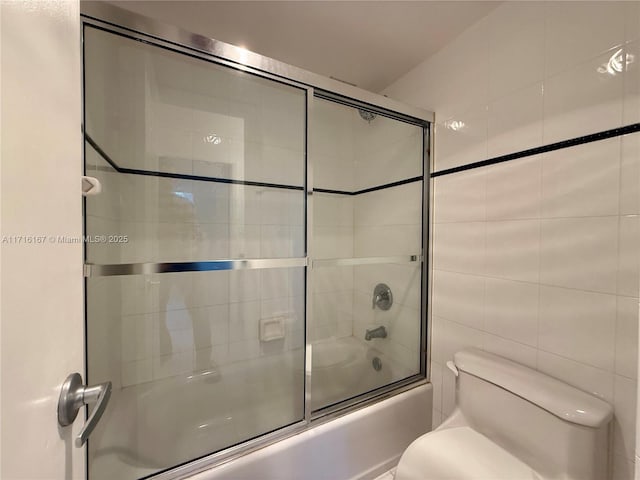 bathroom featuring toilet, combined bath / shower with glass door, and tile walls