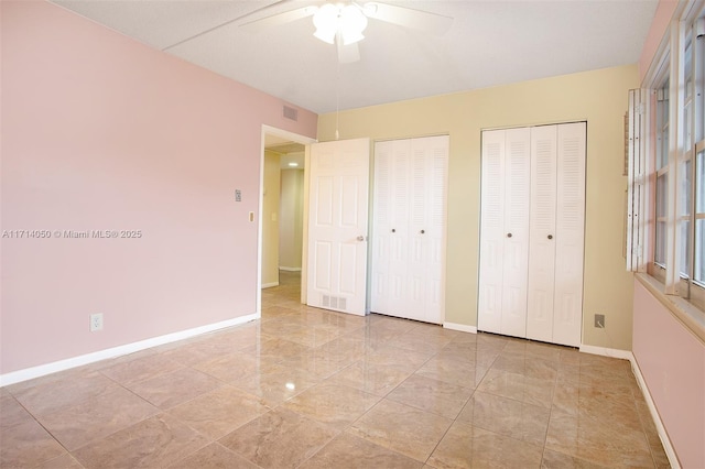 unfurnished bedroom featuring ceiling fan and multiple closets