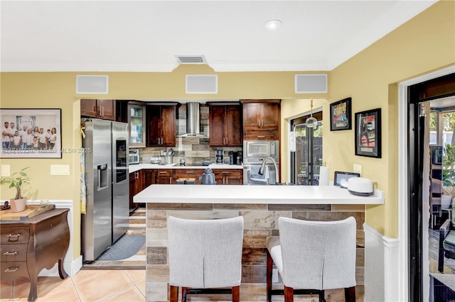 kitchen featuring light tile patterned floors, stainless steel appliances, a kitchen breakfast bar, and wall chimney exhaust hood