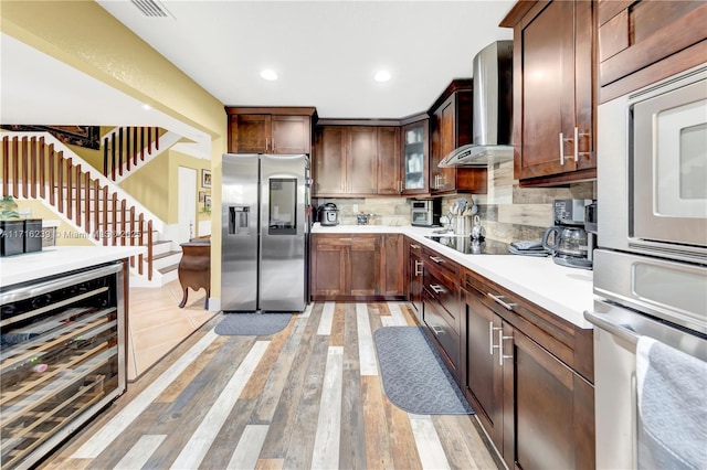 kitchen featuring backsplash, wall chimney exhaust hood, stainless steel appliances, light hardwood / wood-style flooring, and wine cooler