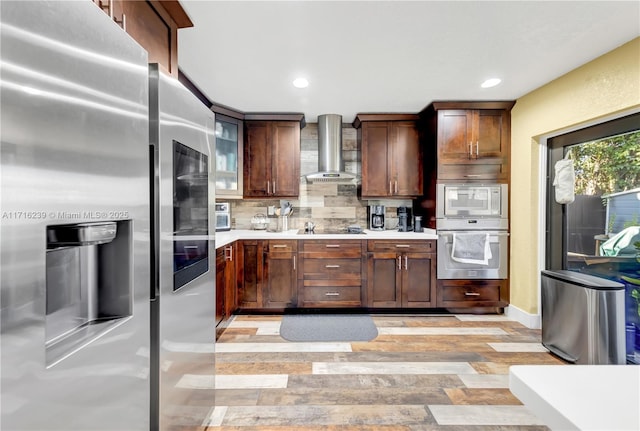 kitchen featuring backsplash, wall chimney exhaust hood, light hardwood / wood-style floors, and appliances with stainless steel finishes