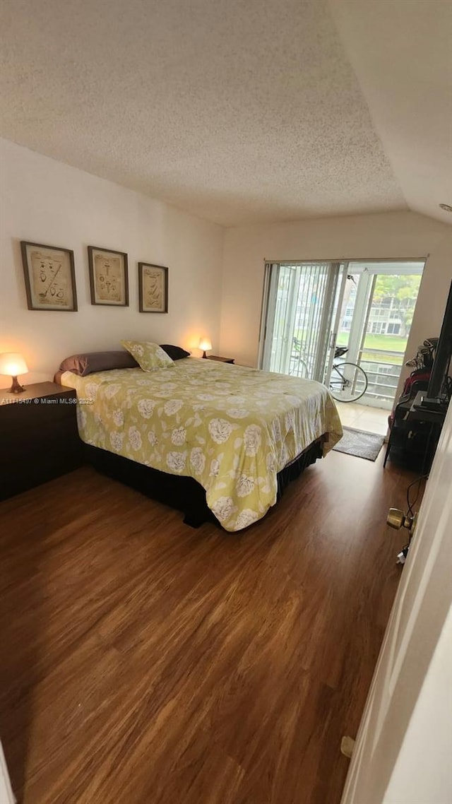 bedroom with a textured ceiling, access to exterior, wood-type flooring, and lofted ceiling