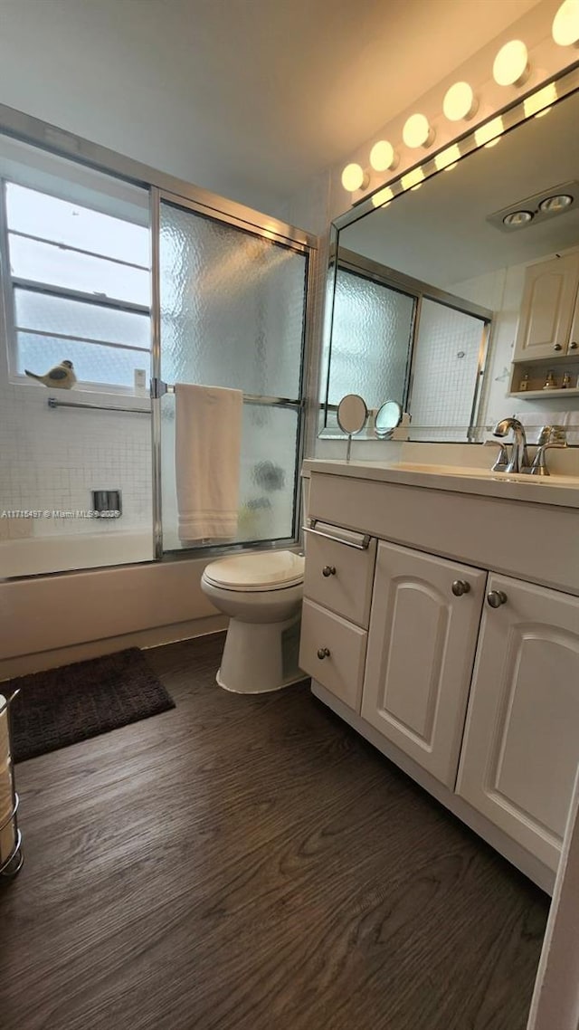 full bathroom featuring hardwood / wood-style flooring, toilet, vanity, and combined bath / shower with glass door