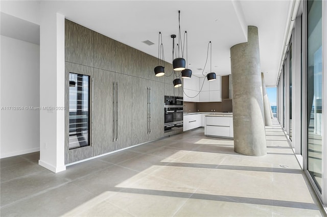 kitchen featuring wall oven, white cabinetry, a towering ceiling, and pendant lighting