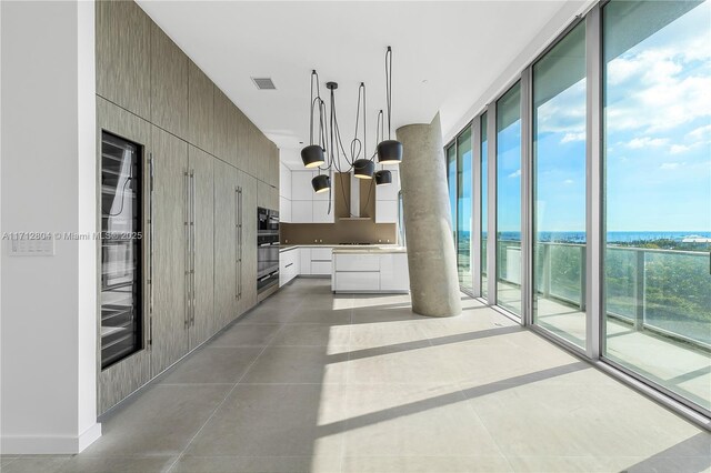 kitchen featuring stainless steel oven, expansive windows, a water view, white cabinetry, and a chandelier