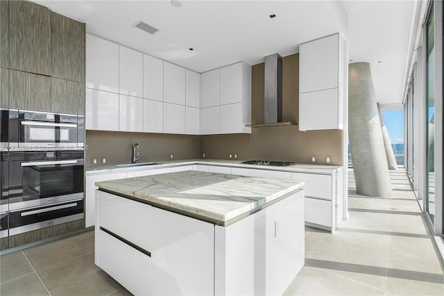 kitchen featuring white cabinets, wall chimney range hood, sink, gas stovetop, and a kitchen island