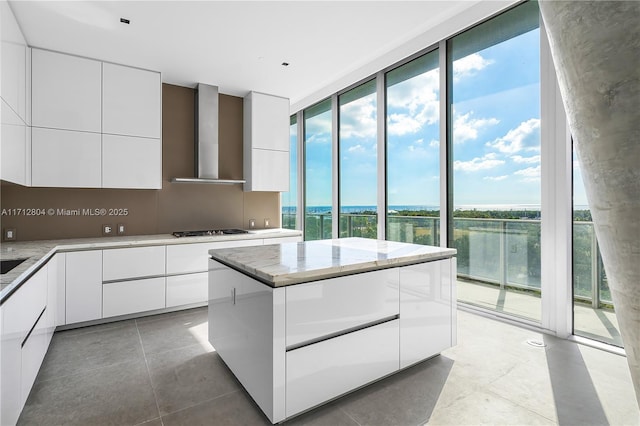 kitchen with white cabinets, a water view, wall chimney exhaust hood, gas stovetop, and a wall of windows