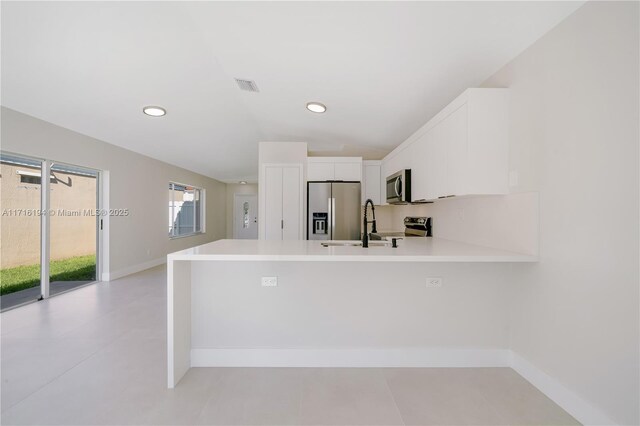 kitchen featuring kitchen peninsula, appliances with stainless steel finishes, vaulted ceiling, white cabinets, and sink