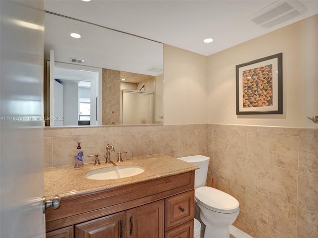 bathroom featuring a shower stall, tile walls, vanity, and visible vents