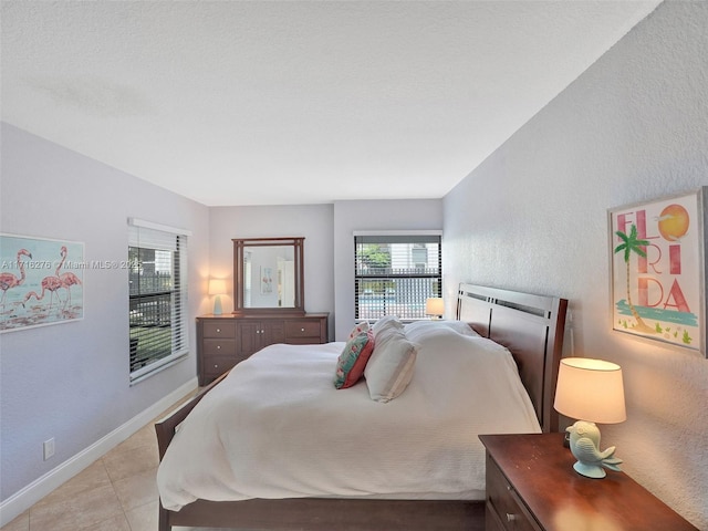 bedroom featuring light tile patterned floors, baseboards, and a textured wall