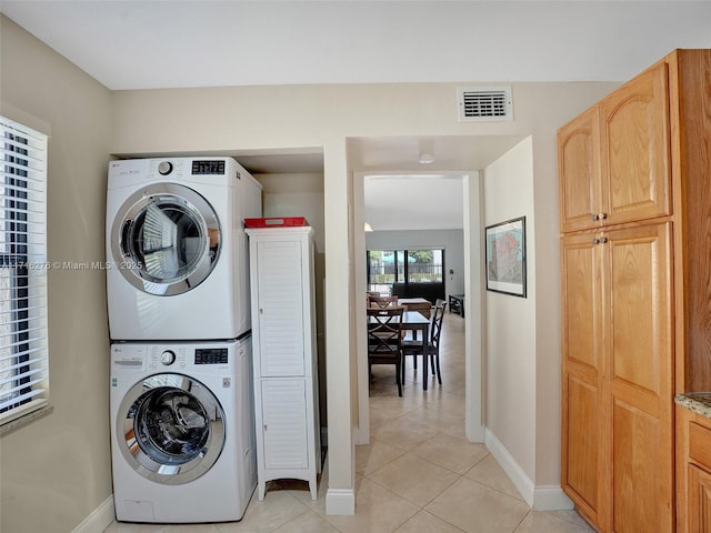 washroom featuring baseboards, visible vents, laundry area, light tile patterned flooring, and stacked washer and dryer