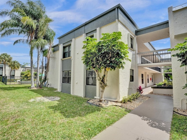 view of side of home with stucco siding, a lawn, and fence